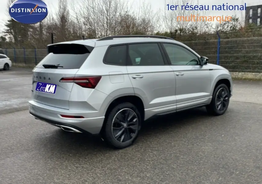 Vue 3/4 arrière droite d'un Skoda Karoq gris argent métallisé avec jantes noires et toit ouvrant panoramique.