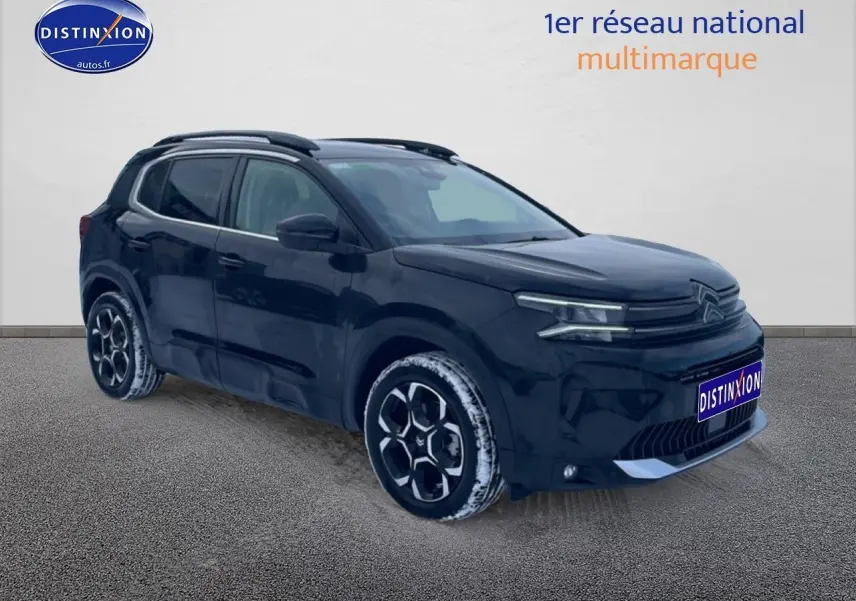 Vue 3/4 avant droit d'un Citroën C5 Aircross noir 2025 avec jantes alu et barres de toit visibles.