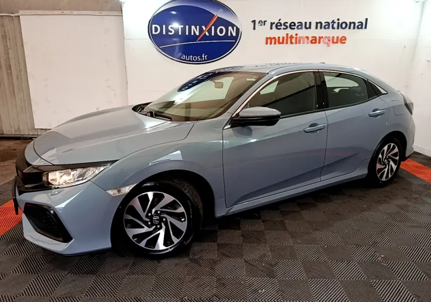 Vue 3/4 avant droit d'une Honda Civic gris clair avec jantes noires et blanches, stationnée en intérieur showroom.