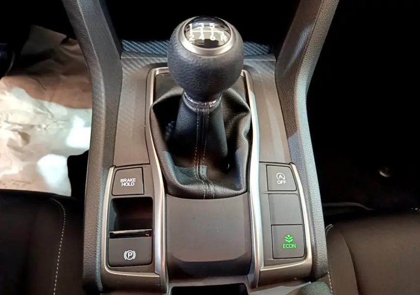 Vue rapprochée du levier de vitesses manuel noir et des boutons de contrôle sur la console centrale d'une Honda Civic gris foncé.