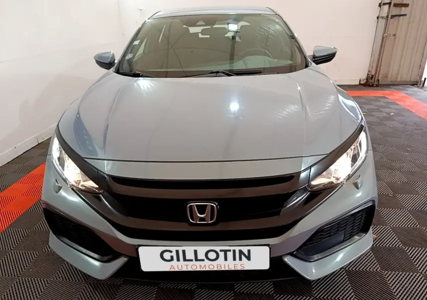 Vue avant frontale d'une Honda Civic 1.0 i-VTEC Exclusive gris foncé avec phares allumés dans un garage.