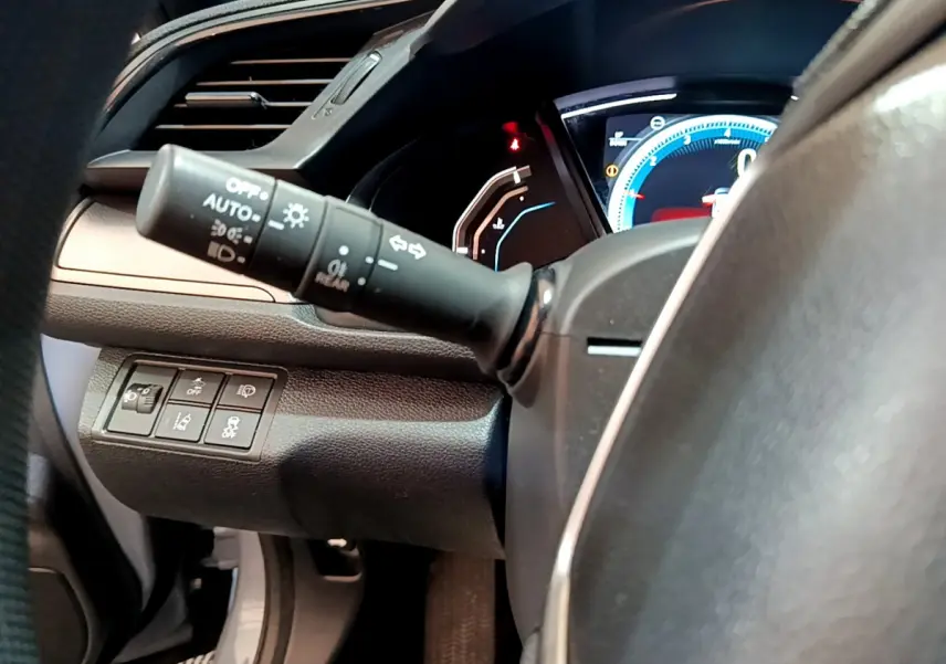 Vue rapprochée du commodo d’éclairage et des commandes au tableau de bord côté gauche dans une Honda Civic 1.0 i-VTEC gris foncé.