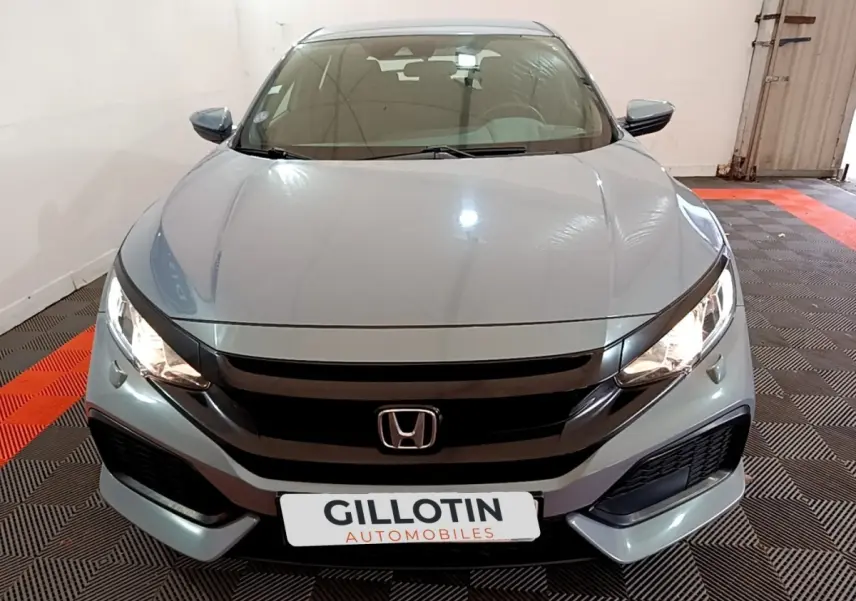 Vue avant d'une Honda Civic 1.0 i-VTEC Exclusive gris foncé avec phares allumés dans un garage.