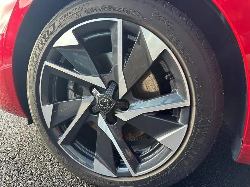 Gros plan sur la jante alliage noire et argentée de la Peugeot 308 SW Rouge Elixir, avec logo Peugeot central visible.