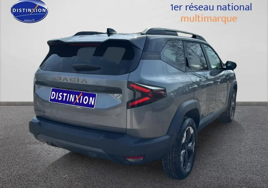 Vue 3/4 arrière droite du Dacia Bigster gris schiste avec feux arrière LED et barres de toit visibles.