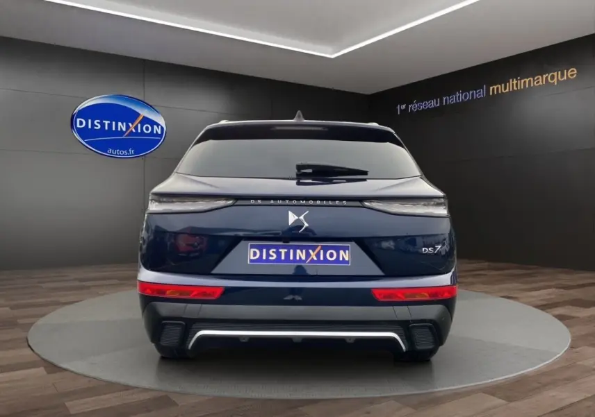 Vue arrière d'un DS7 Crossback bleu 2024 avec feux LED fins et logo DS centré sur un fond showroom.