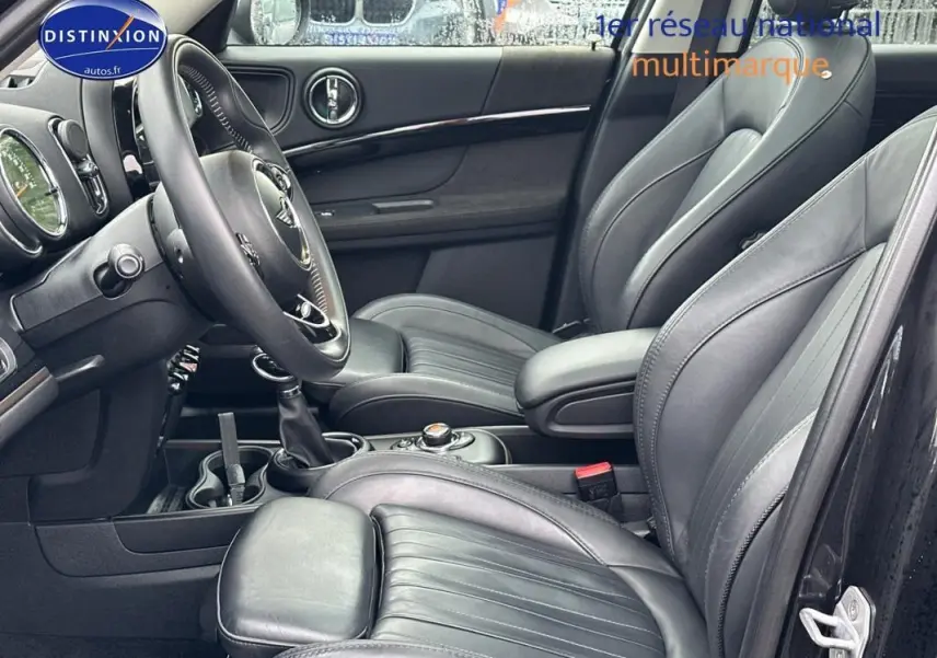 Vue intérieure côté conducteur du MINI Countryman noir, mettant en valeur les sièges cuir et l'accoudoir central.