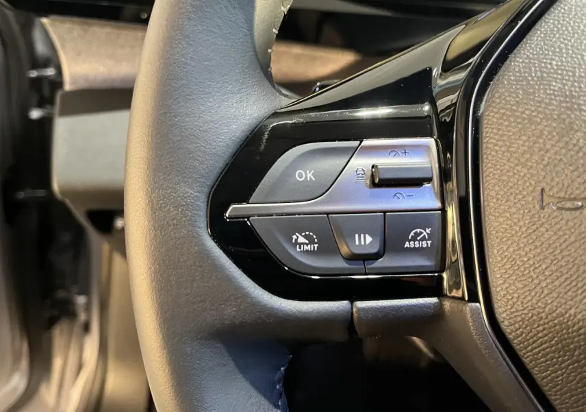 Gros plan sur les commandes à gauche du volant noir du Peugeot 308 SW gris clair Metal Artense 2024.