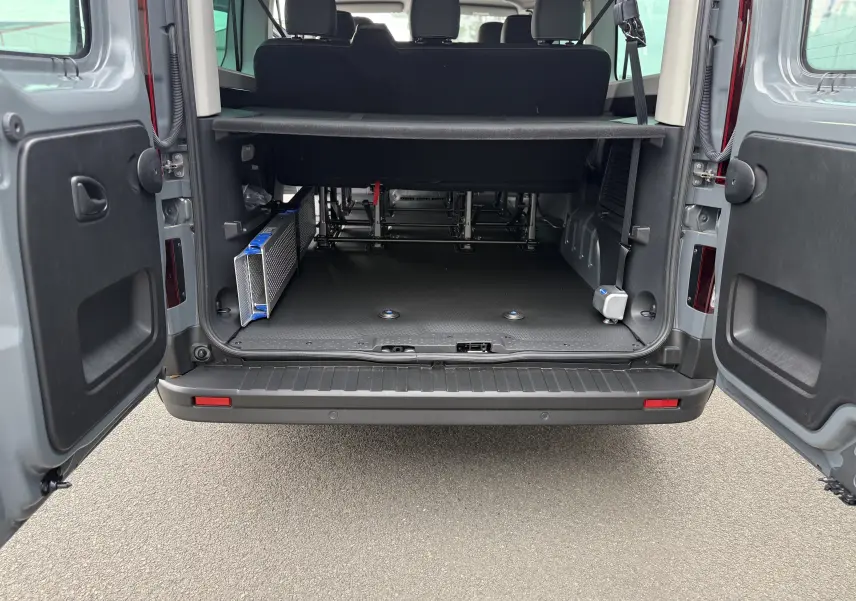 Vue arrière du Renault Trafic Combi gris urbain 2025 avec portes ouvertes montrant l'espace de chargement et l'adaptation pour fauteuil roulant.