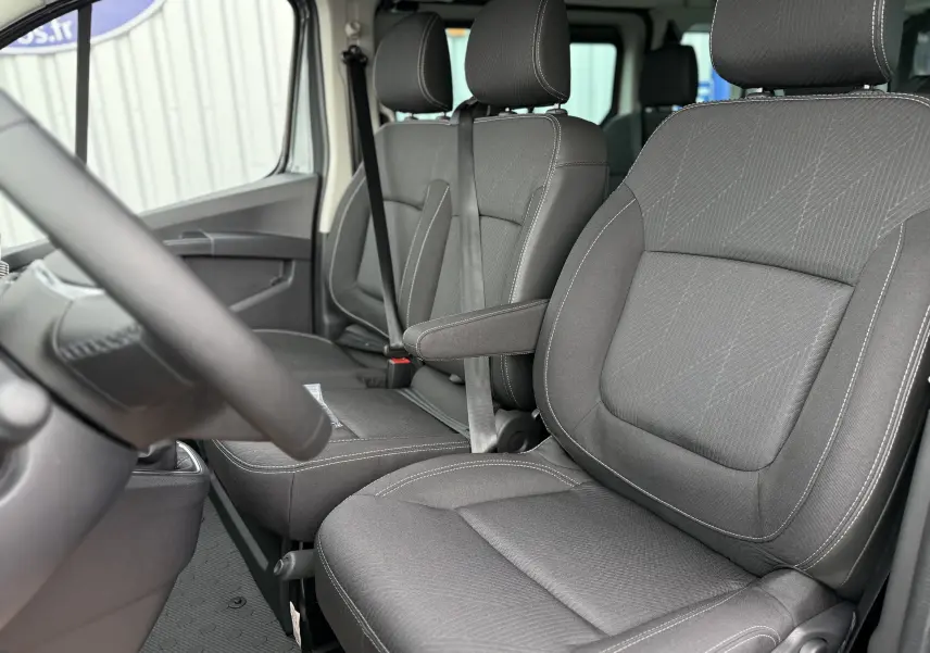 Intérieur du Renault Trafic Combi 2025, vue côté conducteur sur les sièges tissu gris urbain avec accoudoir central.