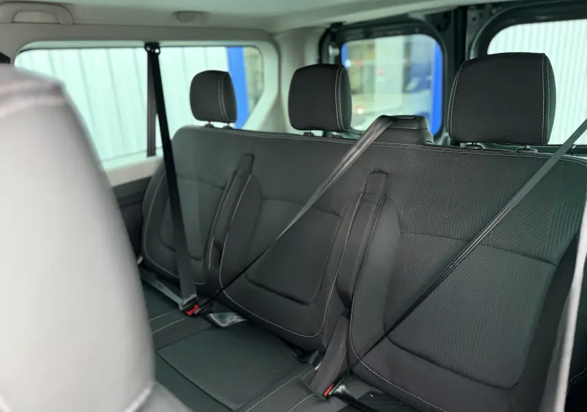 Vue intérieure arrière du Renault Trafic Combi gris urbain 2025, montrant les sièges en tissu noir avec ceintures attachées.