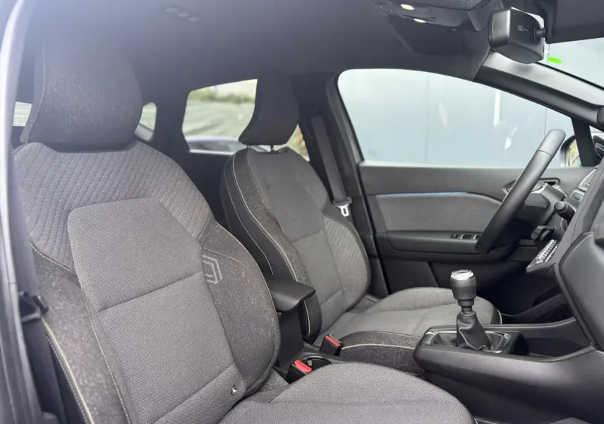 Vue intérieure côté conducteur du Renault Captur 2025, sièges gris avec coutures contrastées et levier de vitesses manuel.