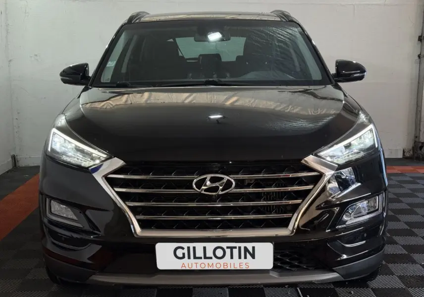 Vue frontale d'un Hyundai Tucson noir 2019 avec calandre chromée et phares LED allumés dans un garage.