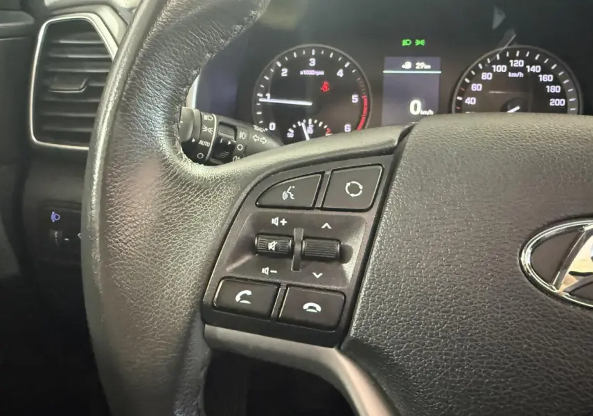 Gros plan sur le volant cuir noir du Hyundai Tucson 2019 avec commandes audio et tableau de bord éclairé.