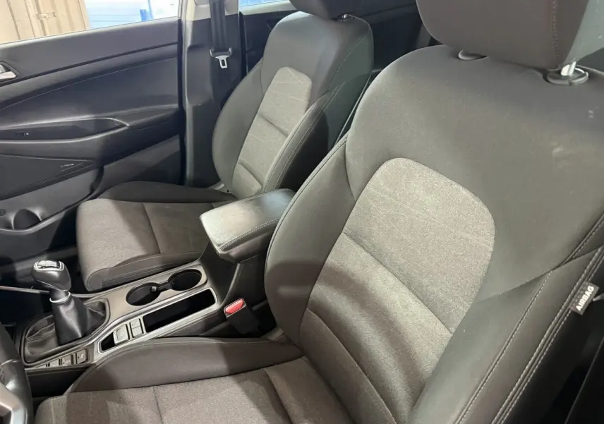 Vue intérieure côté conducteur du Hyundai Tucson 2019 noir, montrant sièges tissu et levier de vitesses manuelle.