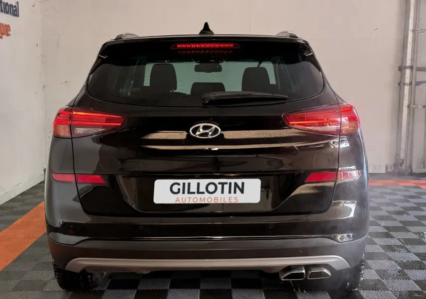 Vue arrière d’un Hyundai Tucson noir 2019 avec feux LED et double sortie d’échappement visible en intérieur showroom.
