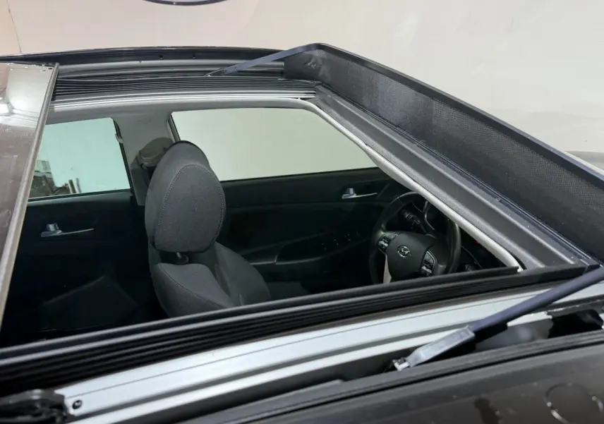 Vue intérieure par le toit ouvrant du Hyundai Tucson noir, montrant siège avant et volant multifonctions.