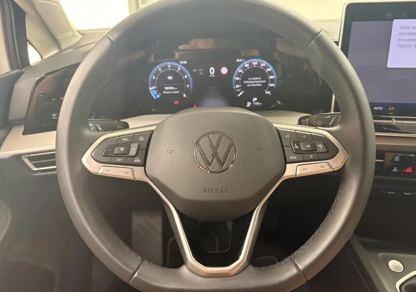 Vue rapprochée du volant noir de la Volkswagen Golf 1.5 eTSI 2025 avec tableau de bord numérique allumé.