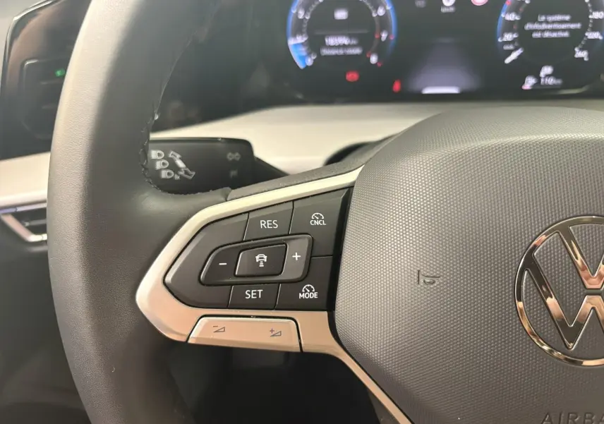 Gros plan sur le volant de la Volkswagen Golf 1.5 eTSI 2025, montrant les commandes de régulateur et le logo VW central.
