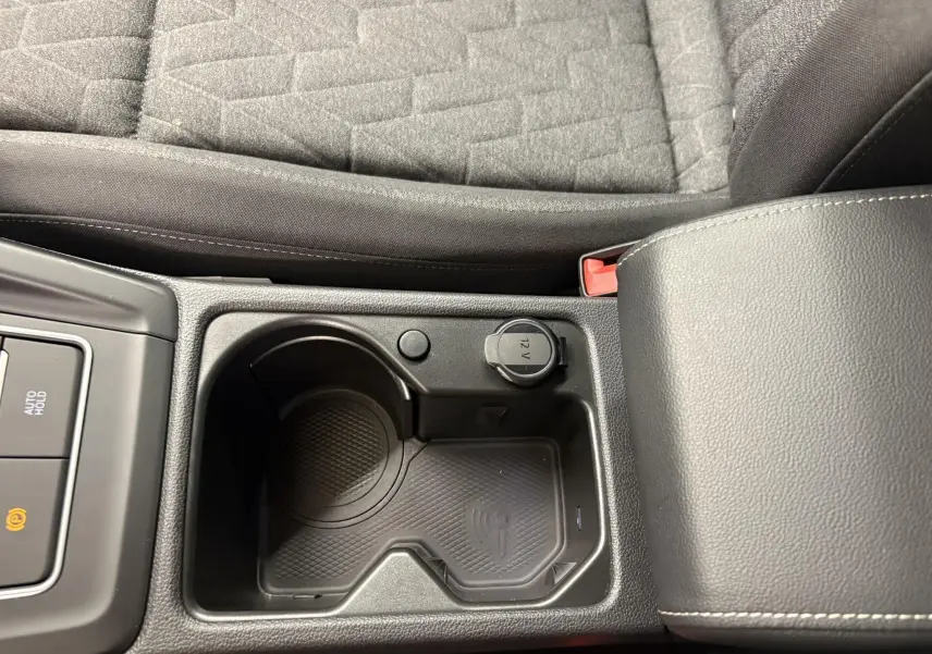 Gros plan sur la console centrale noire avec porte-gobelets, prise 12V et accoudoir en cuir gris de la Volkswagen Golf 2025.