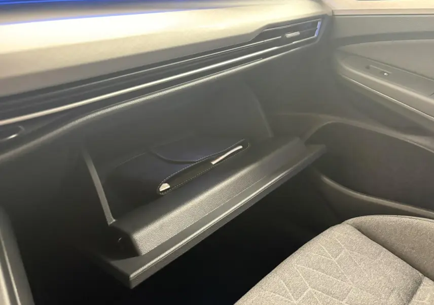 Vue intérieure du coffre à gants ouvert côté passager d'une Volkswagen Golf 1.5 eTSI blanche, avec un livret noir à l'intérieur.