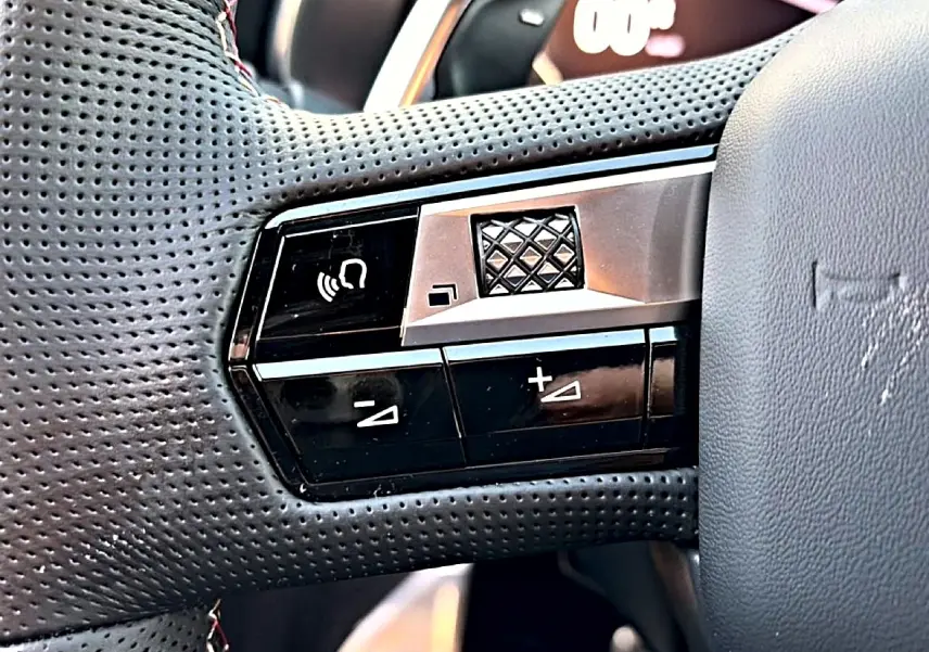 Gros plan sur les commandes gauche du volant en cuir perforé du DS7 noir, avec molette et boutons de réglage sonore.