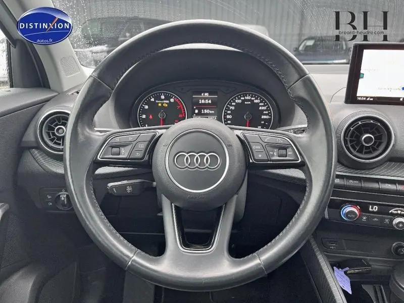 Vue rapprochée du volant cuir multifonction noir de l'Audi Q2 avec tableau de bord et écran GPS visibles.