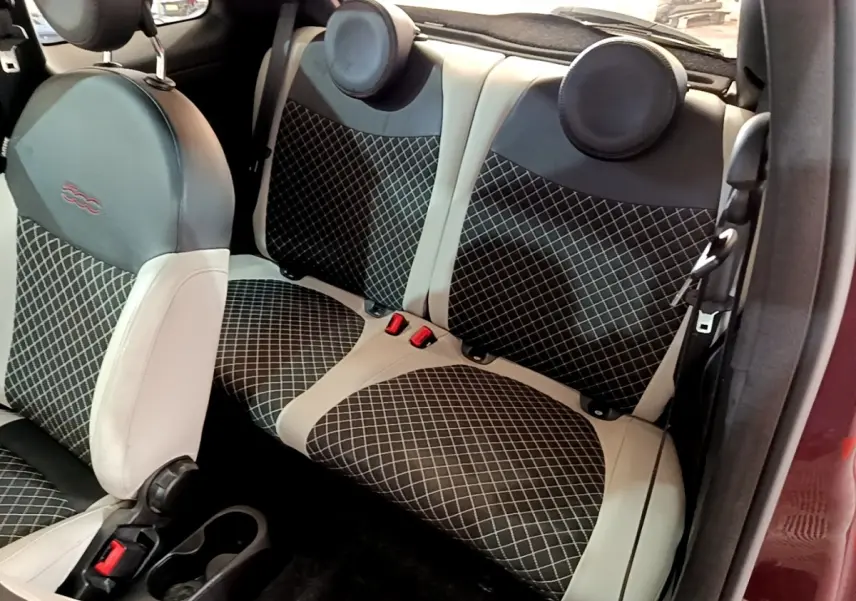 Vue intérieure arrière montrant les sièges arrière en tissu noir à motifs blancs et cuir beige d'une FIAT 500 rouge.