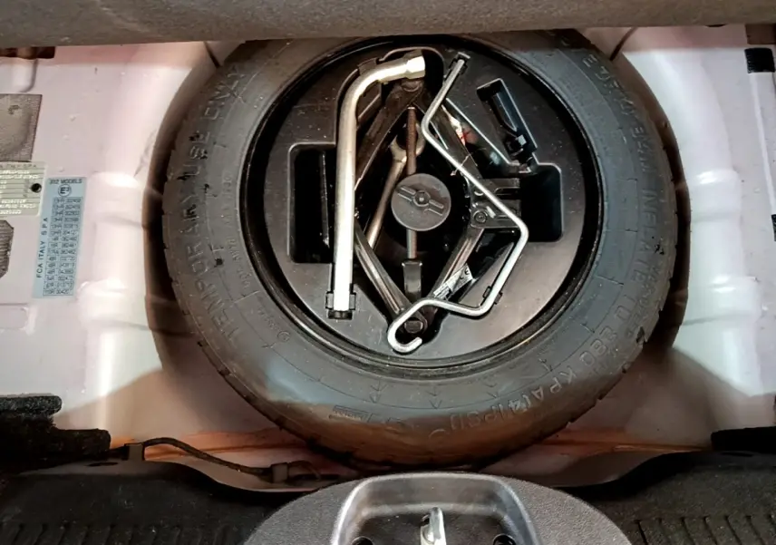 Vue rapprochée de la roue de secours et des outils de bord dans le coffre d'une FIAT 500 rouge.