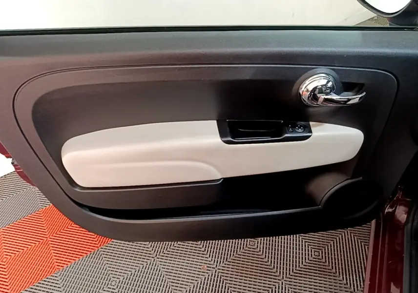 Vue rapprochée de la porte avant droite d'une FIAT 500 rouge, avec poignée chromée et panneau intérieur bicolore noir et beige.