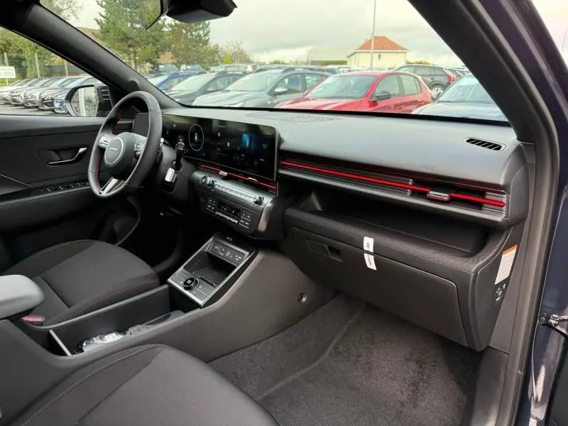 Vue intérieure côté passager du Hyundai Kona 2025 en Cyber Gray, avec tableau de bord noir et bande décorative rouge.