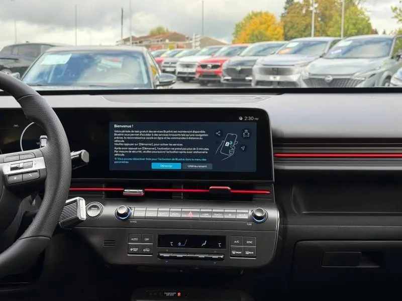 Vue intérieure du tableau de bord de la Hyundai KONA 2025, avec écran tactile et bandeau rouge décoratif.