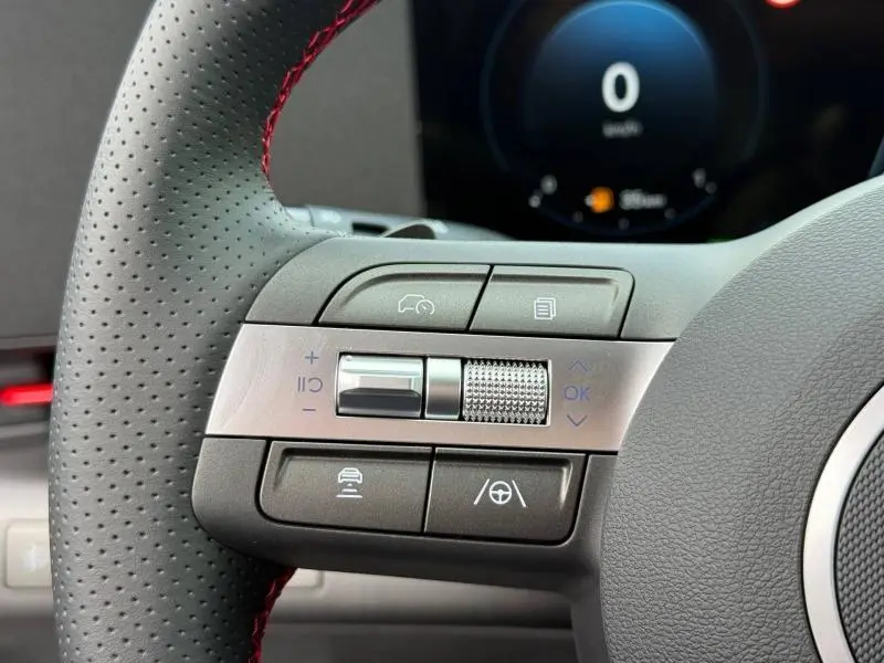 Gros plan sur les commandes multifonctions à gauche du volant cuir perforé rouge du Hyundai Kona Cyber Gray 2025.