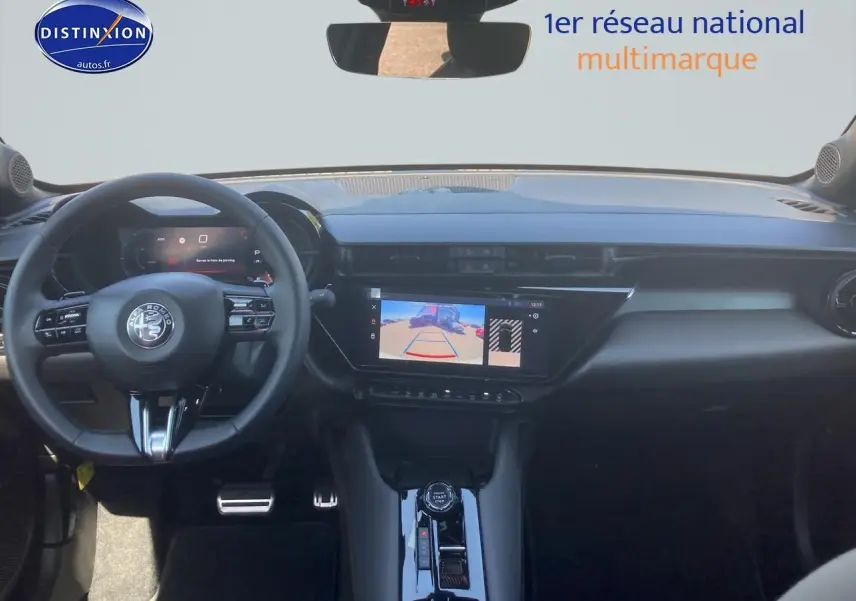 Vue intérieure avant de l'Alfa Romeo Junior 1.2 hybride ivoire et noir, avec tableau de bord numérique et écran tactile affichant la caméra de recul.