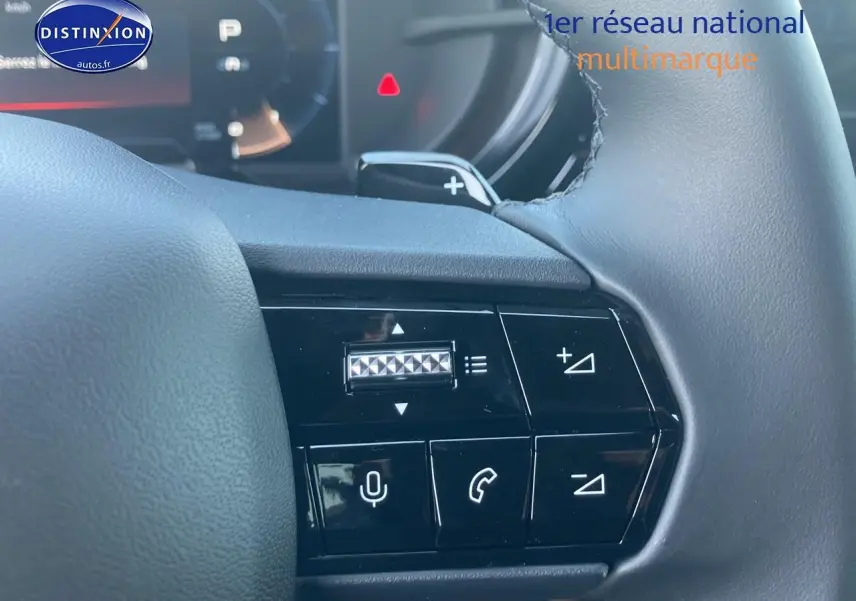 Gros plan sur les commandes au volant à droite de l'Alfa Romeo Junior 1.2 hybride ivoire et noir, avec tableau de bord numérique en arrière-plan.