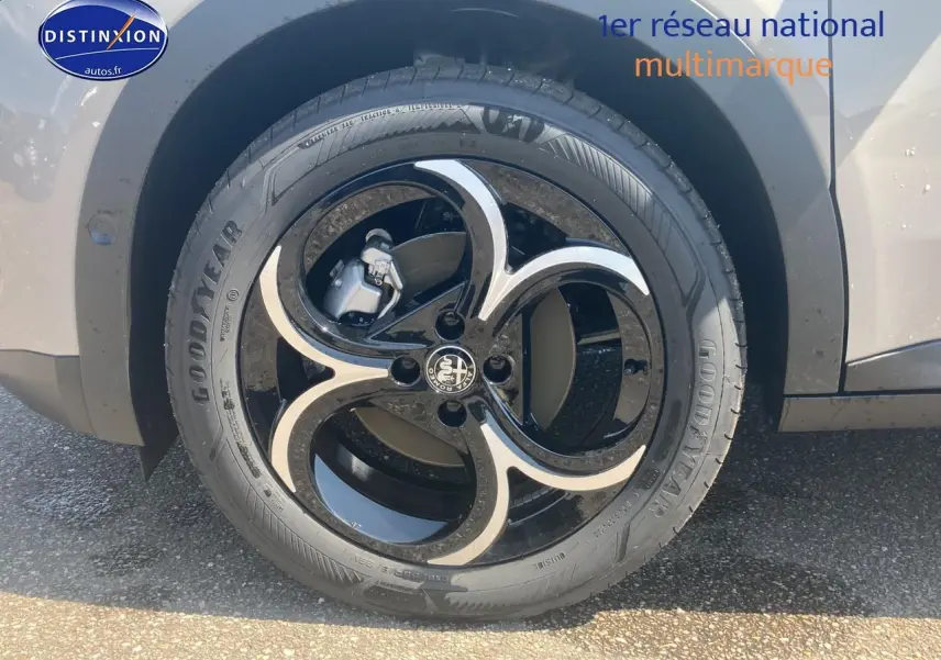 Gros plan sur la jante en alliage noire et ivoire de l'Alfa Romeo Junior 1.2 hybride, avec pneu Goodyear visible.