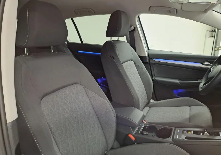 Vue intérieure de profil droit des sièges avant gris foncé de la Volkswagen Golf 1.5 eTSI 116 DSG7 avec éclairage d'ambiance bleu.