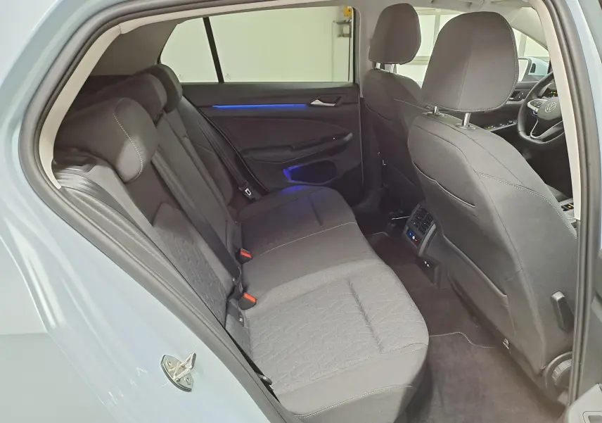 Vue intérieure arrière droite de la Volkswagen Golf 1.5 eTSI 116 DSG7 Bleu Glacier, sièges tissu gris et éclairage d'ambiance bleu.
