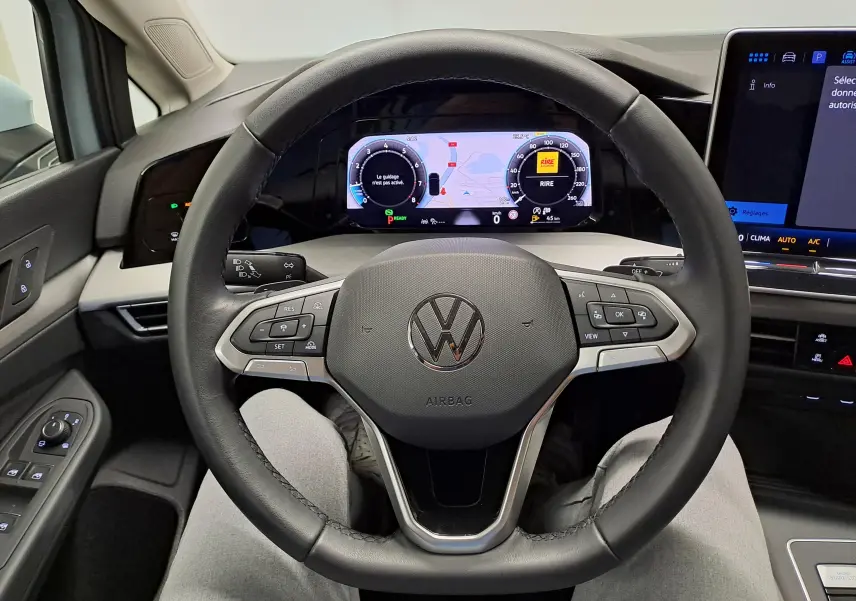 Vue intérieure centrée sur le volant multifonction d'une Volkswagen Golf 2025, tableau de bord numérique visible.