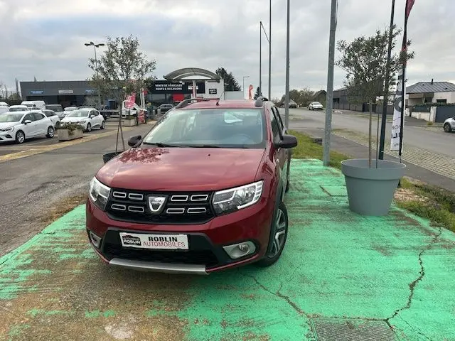 Vue 3/4 avant d'une Dacia Logan MCV rouge 2019 avec calandre noire et jantes alliage, stationnée sur un sol vert.