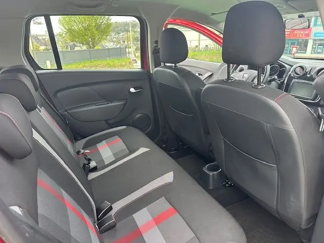 Vue intérieure arrière côté gauche de la Dacia Logan MCV rouge, montrant les sièges arrière en tissu à motifs gris et rouge.