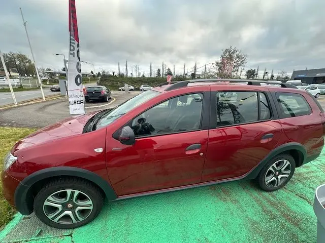 Vue de profil côté gauche d'une Dacia Logan MCV rouge 2019 avec jantes alliage et barres de toit noires.