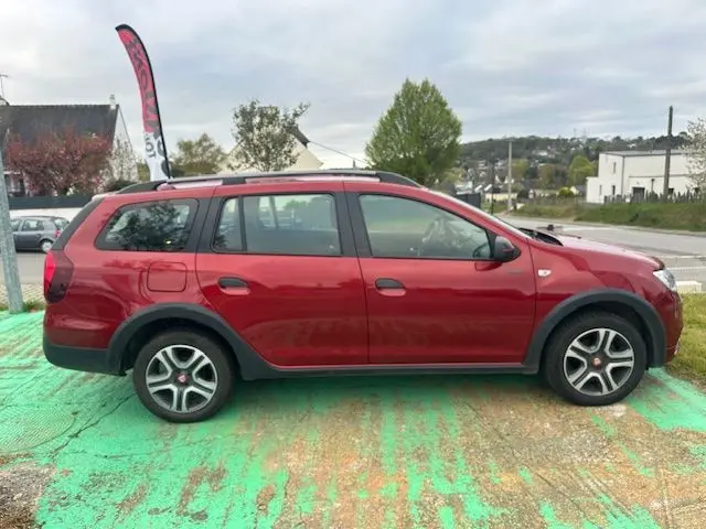 Profil droit d'une Dacia Logan MCV rouge 2019 avec jantes alliage et barres de toit noires sur fond extérieur.