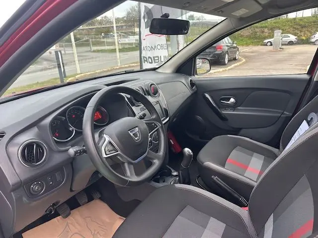 Vue intérieure côté conducteur de la Dacia Logan MCV rouge 2019, avec volant, tableau de bord et sièges gris à bandes rouges.