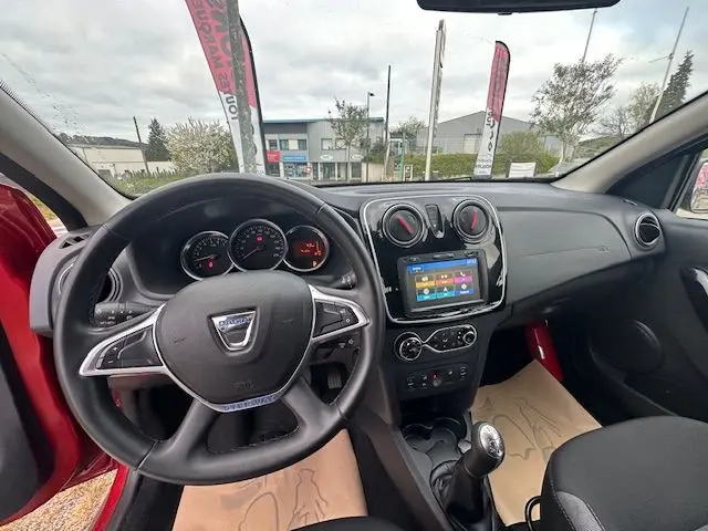 Vue intérieure de face du tableau de bord et volant noir d'une Dacia Logan MCV rouge, avec écran tactile et levier de vitesse manuel.