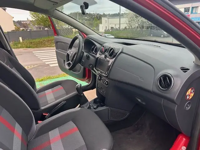 Vue intérieure côté conducteur d'une Dacia Logan MCV rouge 2019, sièges tissu noir avec bandes rouges, tableau de bord simple.