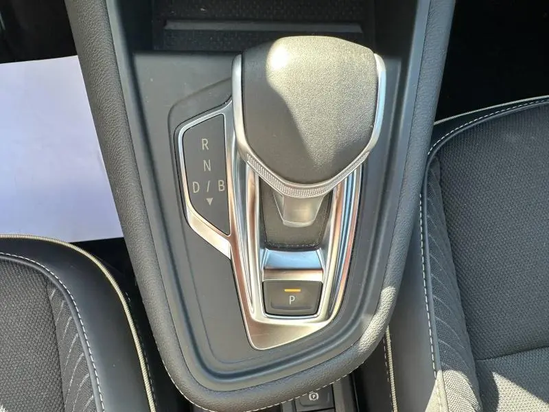 Gros plan sur le levier de vitesses automatique noir et chrome de la Renault Symbioz rouge, entouré de sièges en tissu noir.