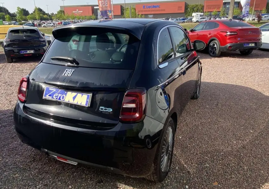 Vue 3/4 arrière droite de la Fiat 500 Electrique noire métal avec badge 500 et prise de recharge visible sur le côté.