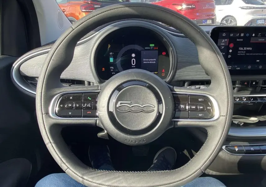 Vue intérieure centrée sur le volant noir de la Fiat 500 électrique avec tableau de bord numérique et écran tactile.