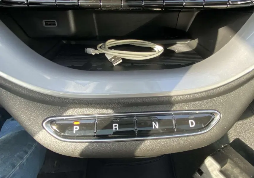 Gros plan sur la console centrale de la Fiat 500 électrique noire, avec les boutons de la boîte auto et un câble USB posé dessus.